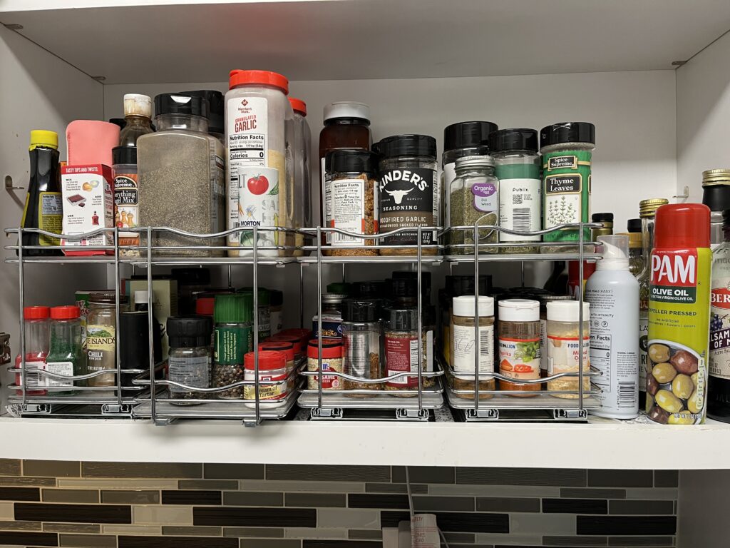 Organize small kitchen spaces with cabinet shelves filled with spices, seasonings, and cooking sprays in metal racks.