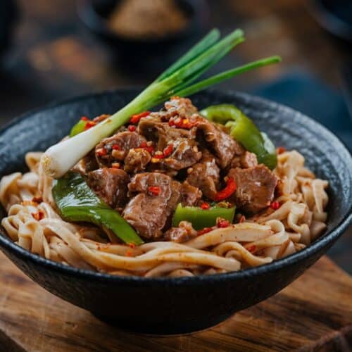 Spicy Beef & Pepper Noodle Bowl with green peppers, chili, and onions served on a wooden board.