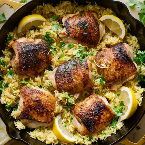 Lemon Herb Chicken & Rice Skillet features golden chicken thighs on seasoned rice, garnished with lemon and parsley.