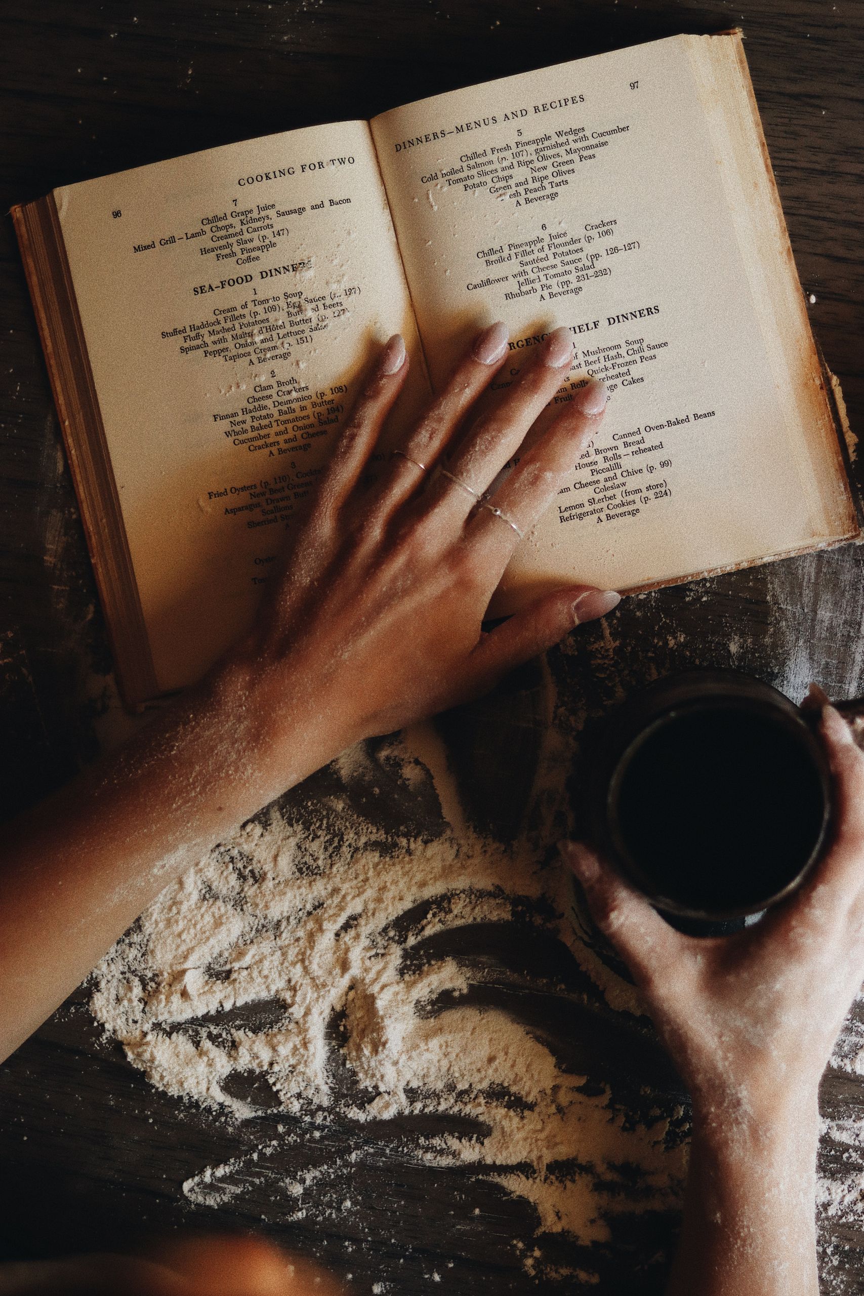 A cozy scene of a person baking bread with a coffee and open cookbook on a flour-covered surface.