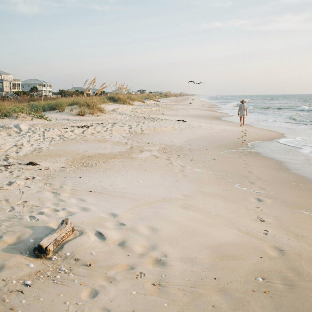 Person walking alone on sandy beach near ocean; Myrtle Beach vacation guide inspires tranquil footprints and soaring birds.